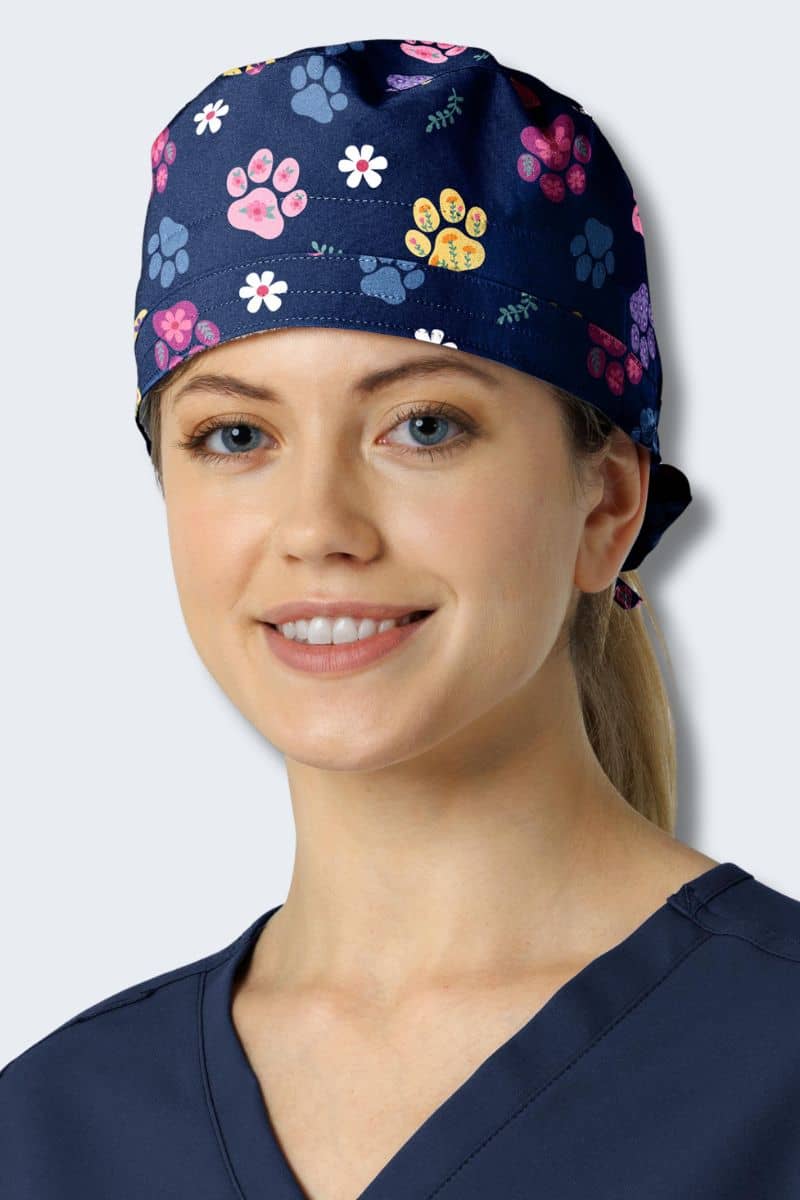 Person wearing a navy blue scrub cap with colorful paw print pattern on a plain background