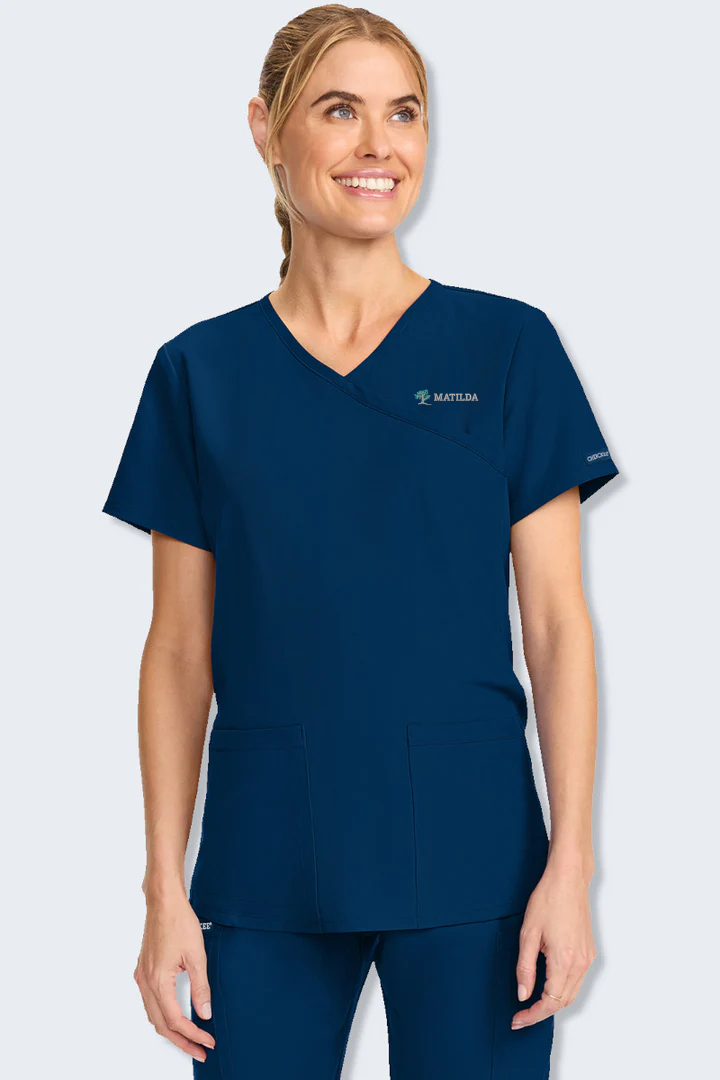 Woman wearing a navy blue scrub top with a visible brand logo on a light gray background