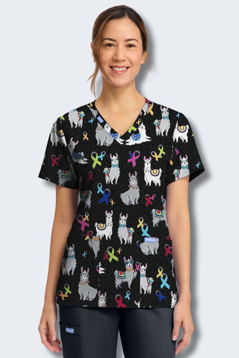 Woman wearing a black scrub top with colorful animal and ribbon pattern on a light gray background. Cherokee CK856_LBMA