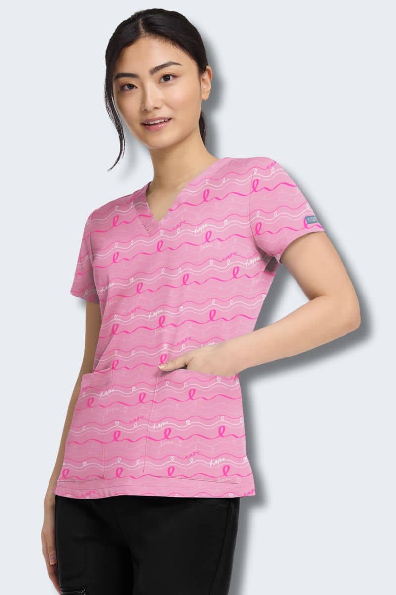 Woman wearing a pink scrub top with breast cancer awareness ribbons on a light gray background. Med Couture MC8564_INOO In the Loop