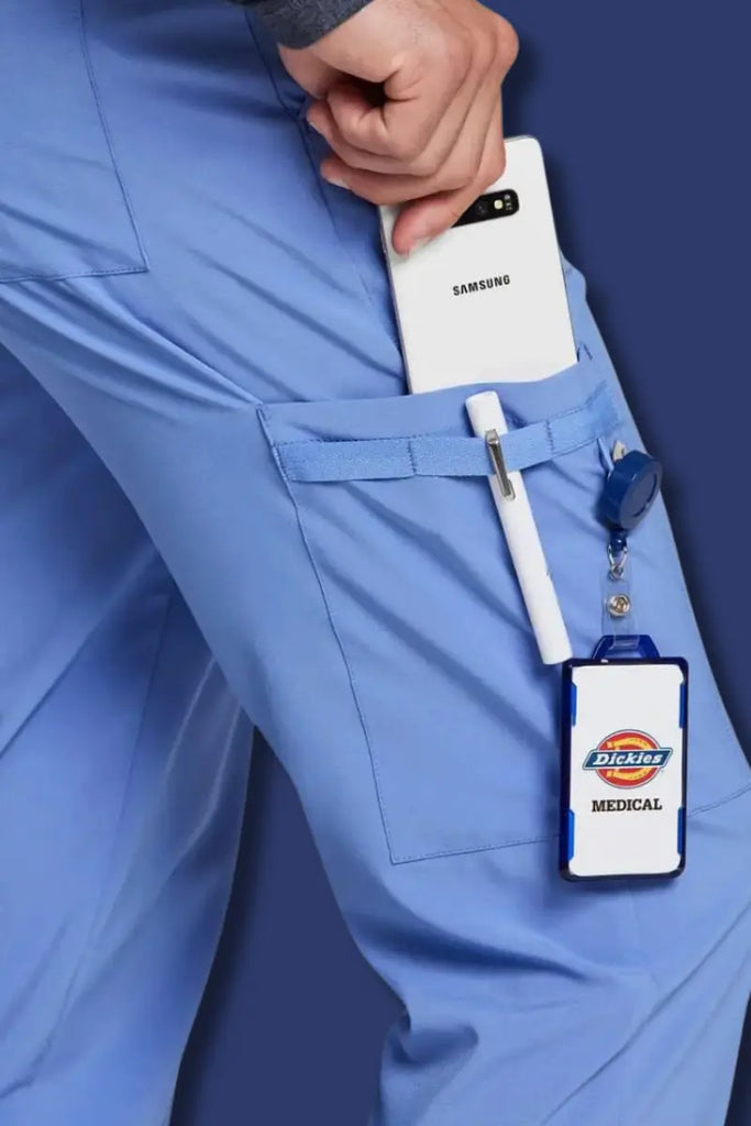 Person wearing blue scrubs with a smartphone, pen, and Dickies Medical badge holder.