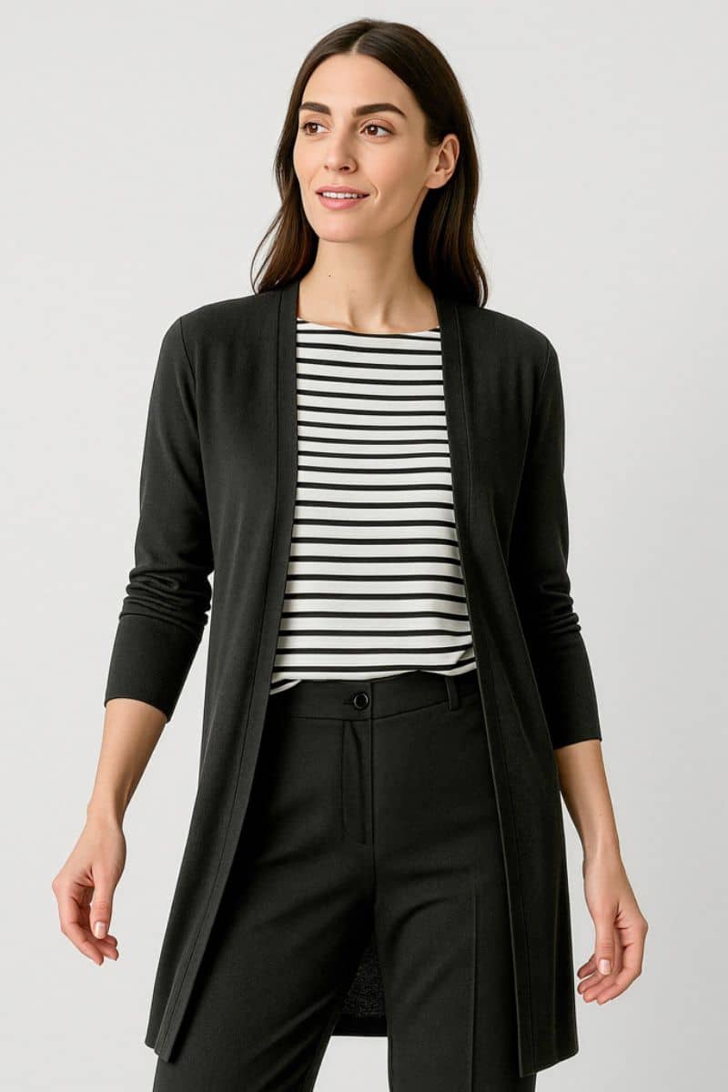 Woman wearing a black cardigan over a striped shirt with black pants on a light gray background